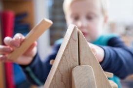 Gutt på ca. fem år som leker med treklosser. Vi ser treklossene i front foran gutten