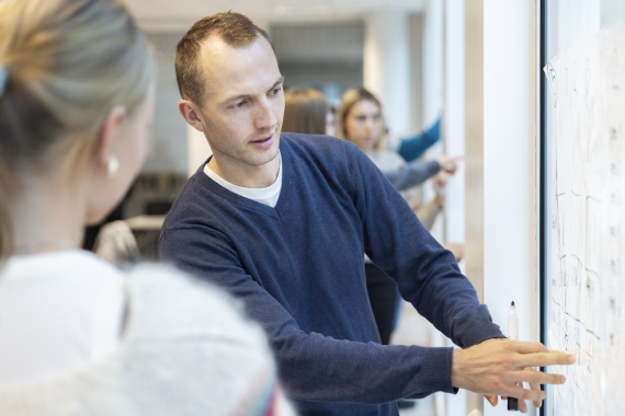 To lærere som står og diskutere ved en vertikal tavle