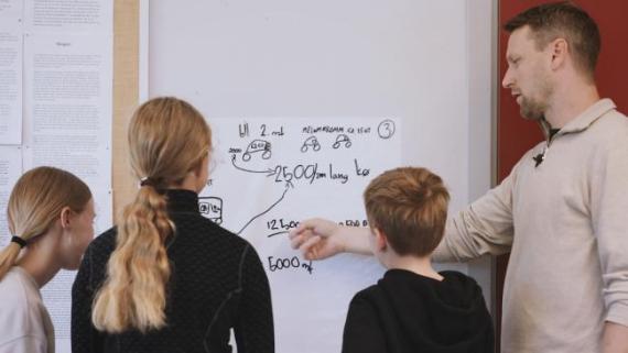 Lærar viser tre elever modellering på tavla.