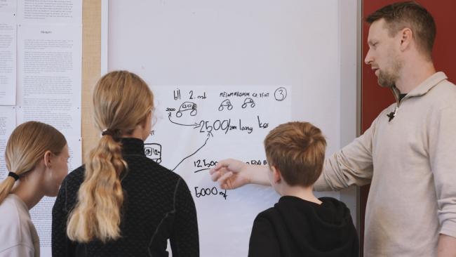 Lærar viser tre elever modellering på tavla.